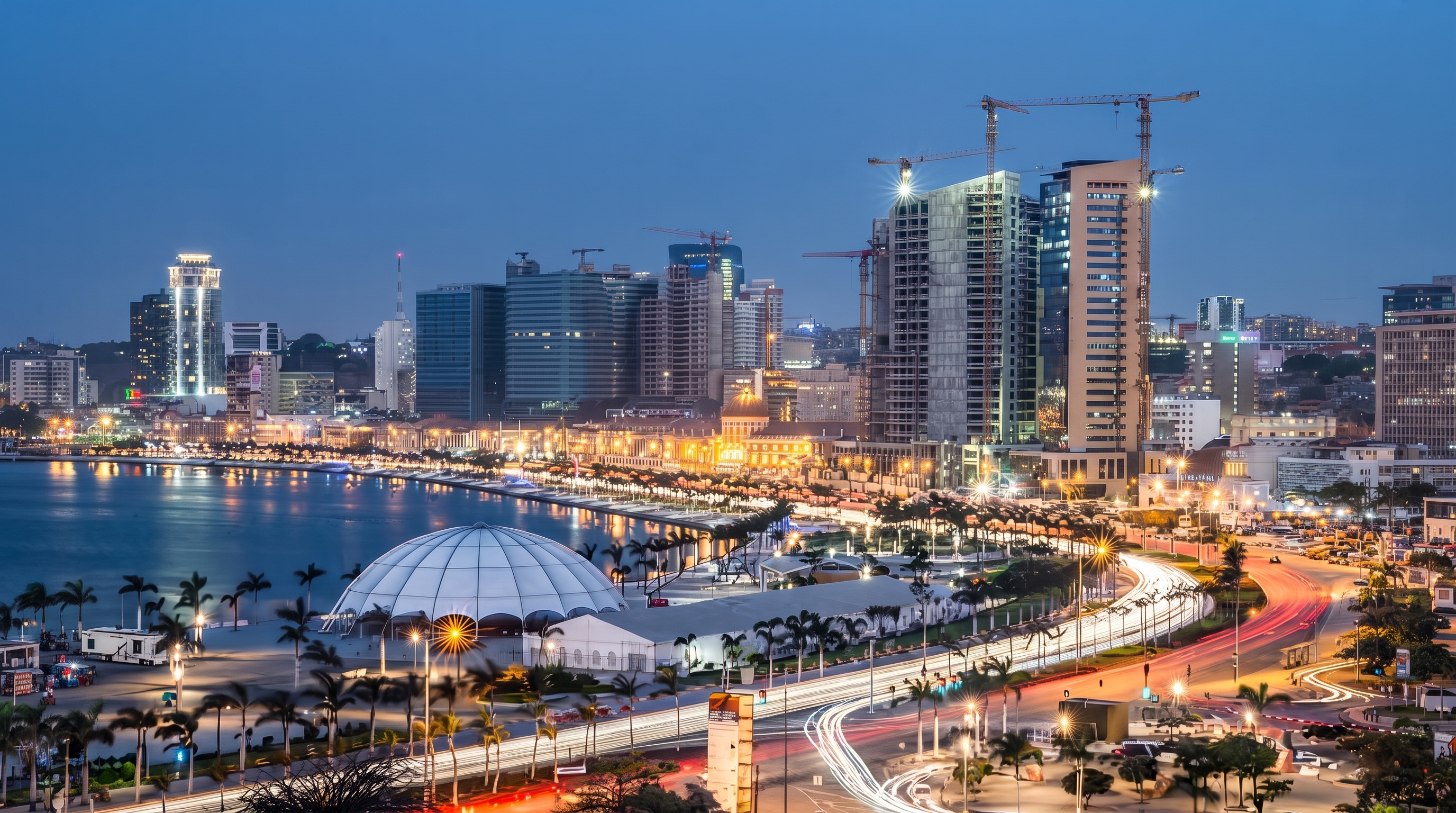 Skyline da Marginal de Luanda ao anoitecer, com arranha-céus e gruas de construção